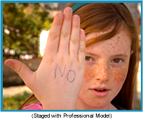 Red-headed girl with her right hand in front of her with the word "no" written on it in blue (staged with professional model).