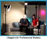 TV studio with two people sitting on a couch highlighted by floodlight. (Staged with professional models.)