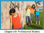 Group of young girls laughing, whispering, and pointing at a girl whose head is hung in shame. (Photo staged with professional models).