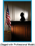 Silhouette of man in witness box in a courtroom with American flag on floor pole.