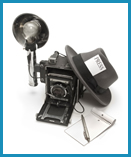 Black and white picture of old fashion camera with traditional press hat resting against it.