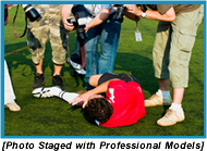 Press photographers taking pictures of an injured man laying on the ground holding his leg. (Photo staged with professional models).